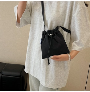 Detail of a large black nylon drawstring bucket bag worn as a crossbody style