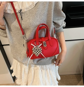 Détail du sac Boston en cuir rouge grainé avec breloque coeur et nœud blanc