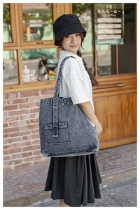 Detail of blue denim tote bag with decorative pockets against a rustic red brick wall