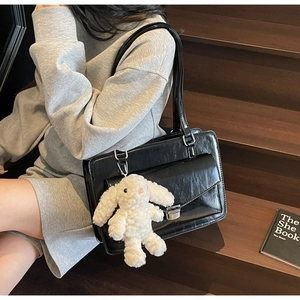 Détail d'un sac messager vintage noir avec boucle en métal et pendentif lapin blanc