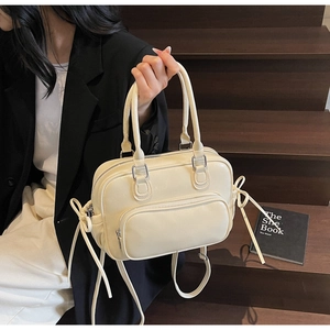 Chic cream bow shoulder bag showcased by a model on wooden stairs for a stylish look