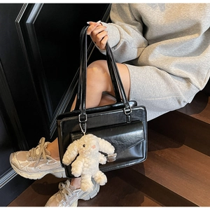 Détail d'un sac cabas noir en similicuir avec poche à rabat et breloque lapin en peluche