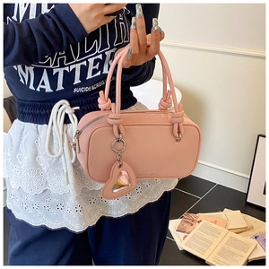 Sac à main rose mat avec poignées nouées et breloque cœur porté par le mannequin