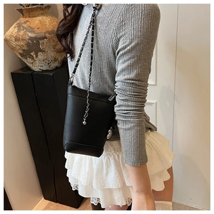 Détail d'un sac seau en cuir grainé noir avec bandoulière chaîne sur un mannequin réel