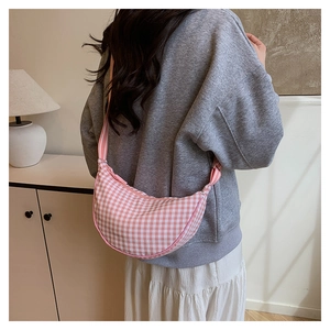 Detail view of pink and white checkered canvas crescent bag worn as a crossbody