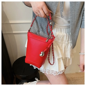 Détail d'un sac seau rouge à texture litchi avec pendentif coeur et bandoulière chaîne