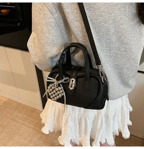 Détail du sac à main en cuir grainé noir avec breloque cœur et bandoulière amovible