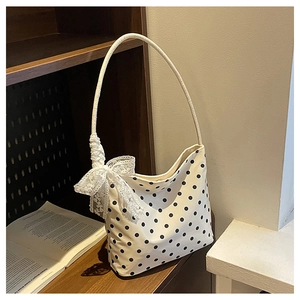 Dettaglio borsa a tracolla a pois con fiocco in pizzo bianco su uno scaffale di legno