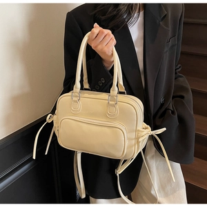 Detail of cream leather pillow bag with drawstring bows and a front zipper pocket