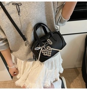 Détail du sac boston en cuir grainé noir avec nœud blanc et pendentif en forme de cœur