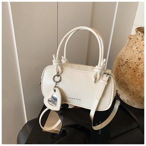 Gros plan du sac oreiller crème avec logo doré et pendentif miroir en forme de cœur