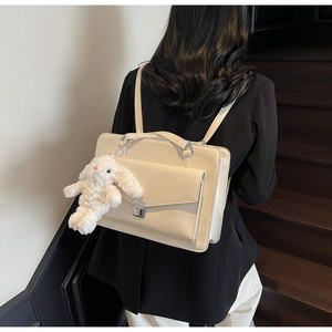 Détail d'un sac à dos carré beige avec boucle en métal argenté et pendentif lapin en peluche