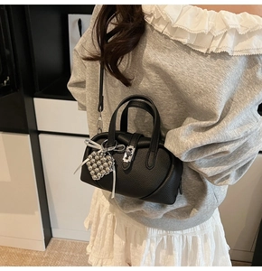 Détail du sac bandoulière en cuir noir avec breloque cœur argentée et ruban blanc