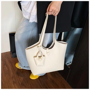 Detail of off-white lychee texture tote bag with matching mini charm on model hand