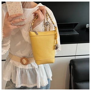 Détail d'un petit sac seau jaune en cuir avec bandoulière chaîne et pendentif en métal