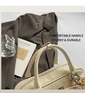 Dettaglio borsa tessuta color crema con manici in pelle e ciondolo fiocco in pizzo