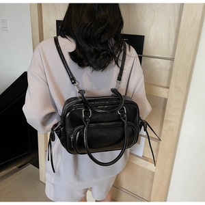 Rear view of a model wearing a shiny black leather backpack with long fringe zipper pulls