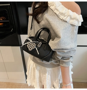 Détail du mini sac Boston en cuir noir avec breloque cœur argentée et nœud blanc