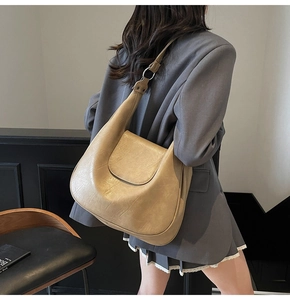 Close-up of khaki dumpling bag in cracked faux leather with metallic hardware and strap
