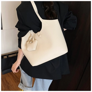 Detail view of large beige pebble leather tote bag with small charm on a black suit