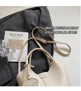 Detail view of cream lychee-textured leather handbag with adjustable long strap on grey blazer