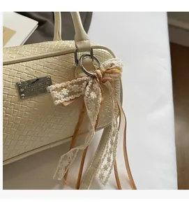 Dettaglio borsa intrecciata beige con ciondolo a fiocco in pizzo e placca logo in metallo