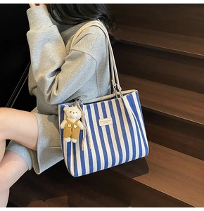 Détail du sac cabas en toile rayée bleue avec anses en cuir sur un escalier en bois