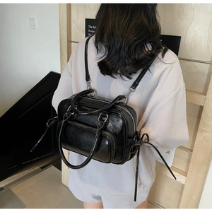 Rear view of a model wearing a shiny black leather multifunctional backpack with silver zippers