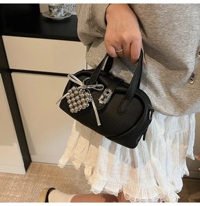 Détail d'un sac Boston en cuir grainé noir avec fermoir argenté et breloque cœur