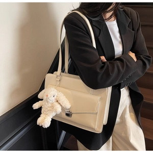 Détail du sac messager crème avec fermoir argenté et breloque lapin en peluche sur blazer
