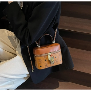 Close-up of brown bucket bag with monogram pattern and gold chain strap on a model