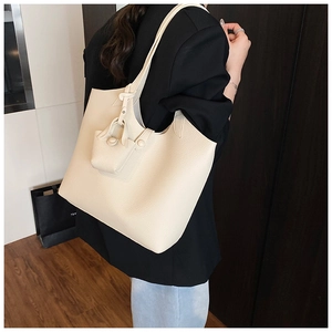 Close-up of cream tote bag with pebble texture, slim straps, and mini coin purse charm