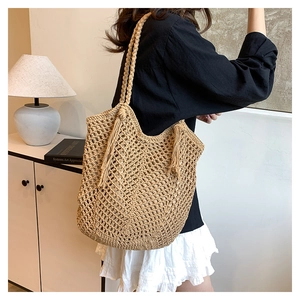 Detail of hollow woven straw tote bag featuring decorative long side tassels and thick strap