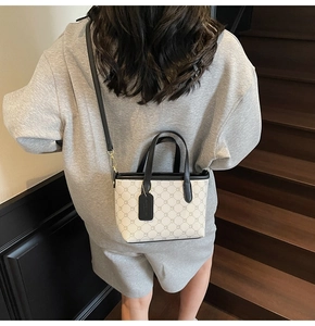 Détail d'un sac seau beige à motifs porté par un mannequin sur un escalier noir