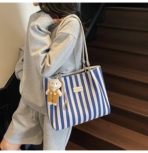 Gros plan du cabas en toile rayée bleue avec logo en cuir et breloque petit ours