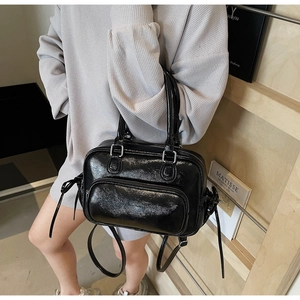 Close-up of black glossy patent leather handbag with silver zippers and top handles