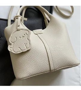 Detail of cream white lychee grain leather bucket bag with cute puppy bag charm