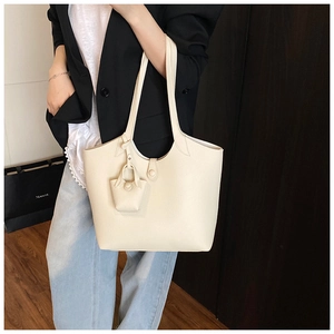 Detail of a beige tote bag with a matching mini pouch charm and lychee leather texture