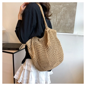 Close-up of handmade hollow straw tote bag with long tassels and woven handles