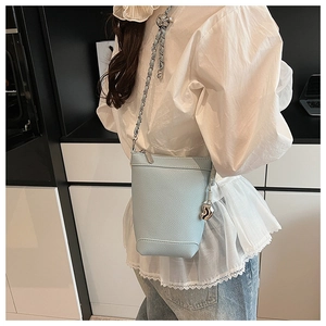 Détail d'un sac seau bleu clair à motif litchi avec chaîne argentée et breloque cœur