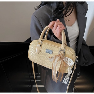 Dettaglio della borsa Boston in pelle beige con fiocco in pizzo e targhetta in metallo