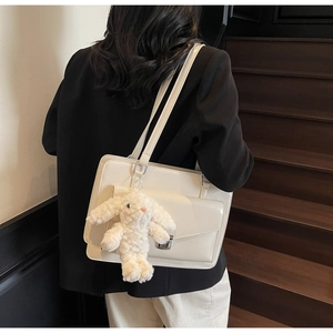 Détail du sac en cuir crème avec boucle argentée et breloque lapin sur un escalier