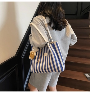 Détail du cabas en toile à rayures bleues avec pendentif ours et anses en cuir blanc