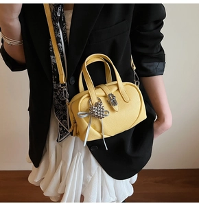 Détail du sac en cuir grainé jaune vif avec pendentif cœur en strass et nœud argenté