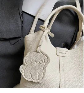 Detail of beige lychee pattern leather bucket bag with cute dog charm and fashion stamp