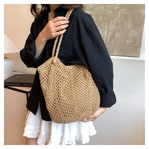 Close-up of hollow straw woven tote bag featuring fringe tassels and natural wood tone texture