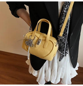 Détail d'un sac bandoulière jaune en cuir grainé avec fermoir argenté et breloque cœur