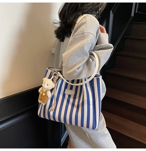 Détail du cabas à rayures bleues avec poignée en cuir blanc et breloque ours en peluche