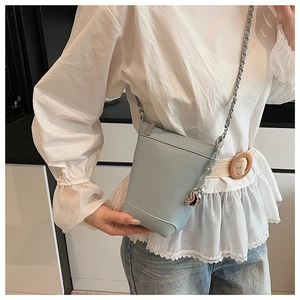Gros plan du sac seau en cuir bleu clair avec bandoulière chaîne porté par un mannequin