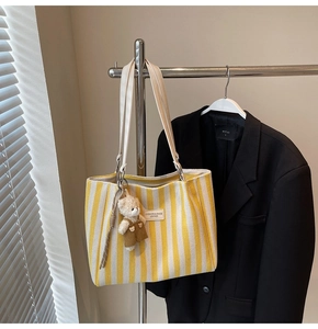 Détail du sac cabas en toile à rayures jaunes et blanches avec breloque d'ours